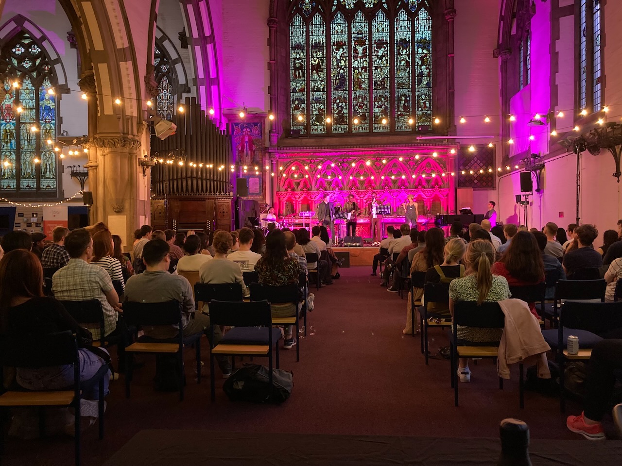 Audience watching The Roots of Jazz in a church lit with pink uplighting