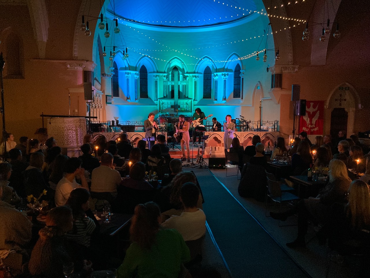 Audience seated around tables for The Roots of Jazz in a blue-lit church