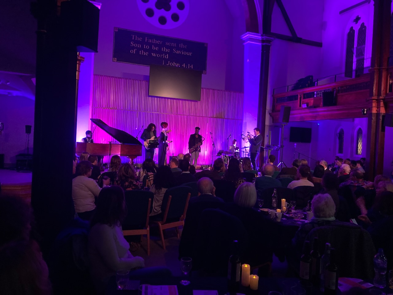 Audience seated at tables during a Roots of Jazz event with purple stage lighting