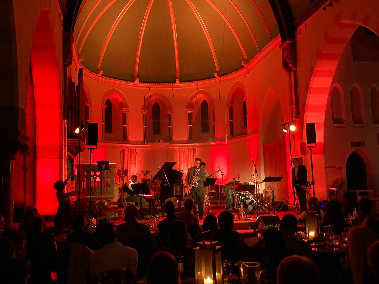 The Roots of Jazz band performing in a round church interior lit red
