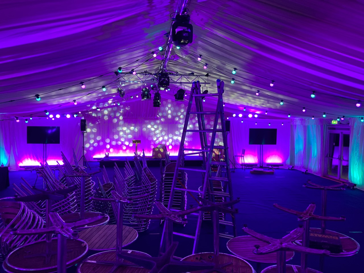 Getting ready for an event, stacks of chairs and a ladder in the foreground, stage lights being tested in the background